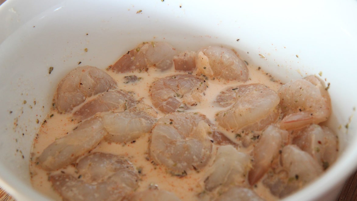 raw shrimp, spices, and milk in a white bowl. 