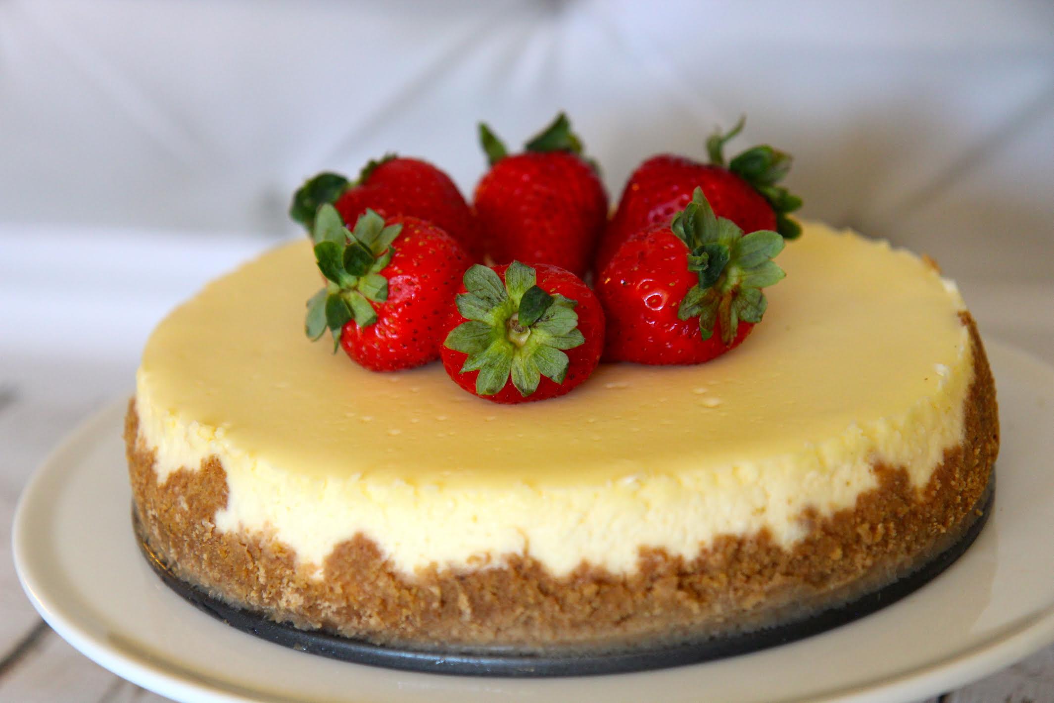 Plain Homemade cheesecake with a graham cracker crust and topped with strawberries.