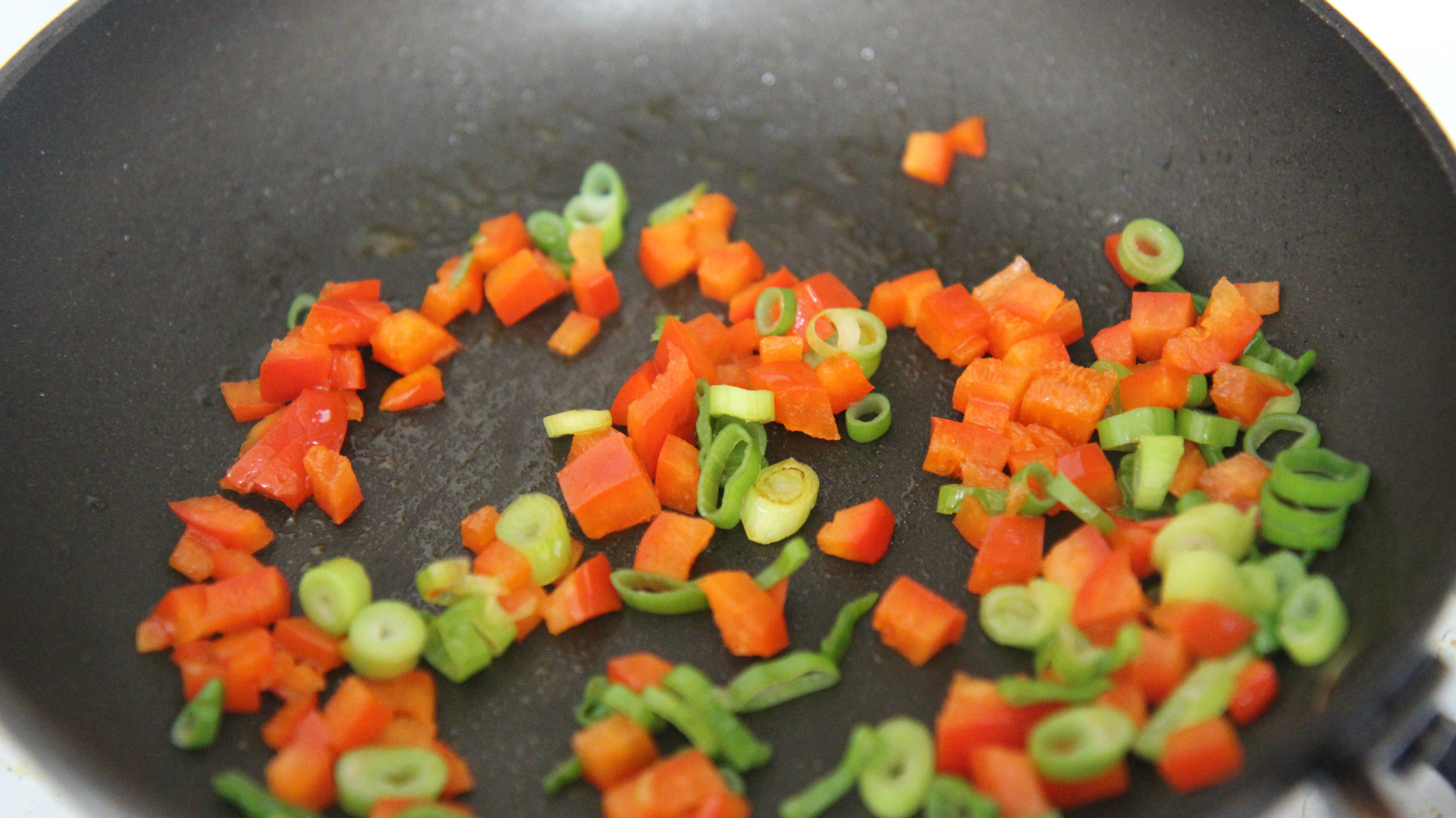 Saute chopped red bell peppers and green onions in a pan. 
