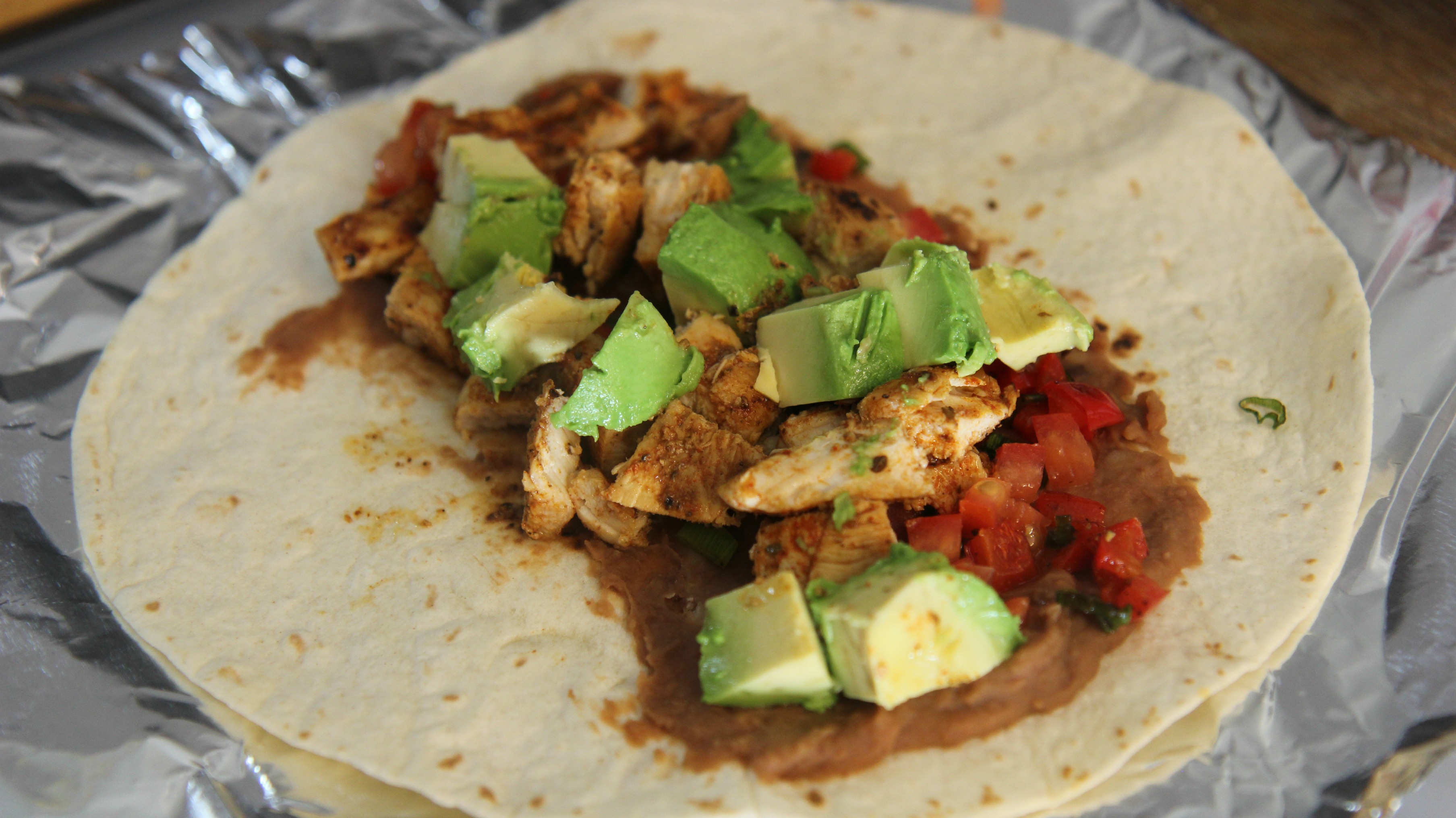 Add the chicken to a tortilla with refried beans, avocado chunks and some tomatoes. 