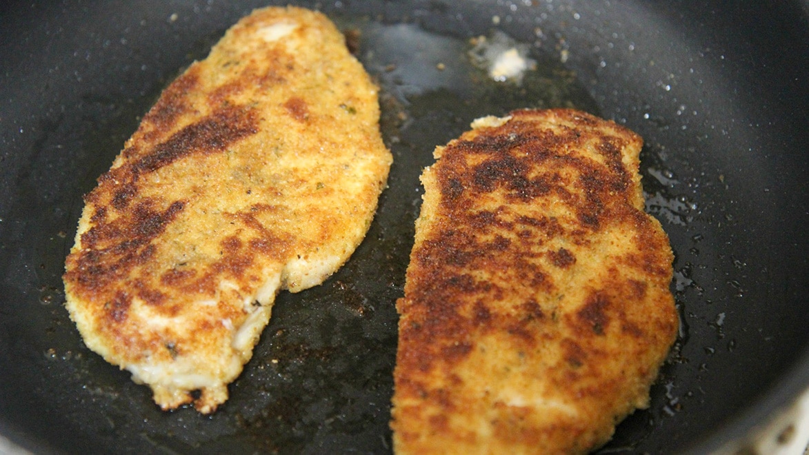 two fried chicken breasts in a black skillet. 