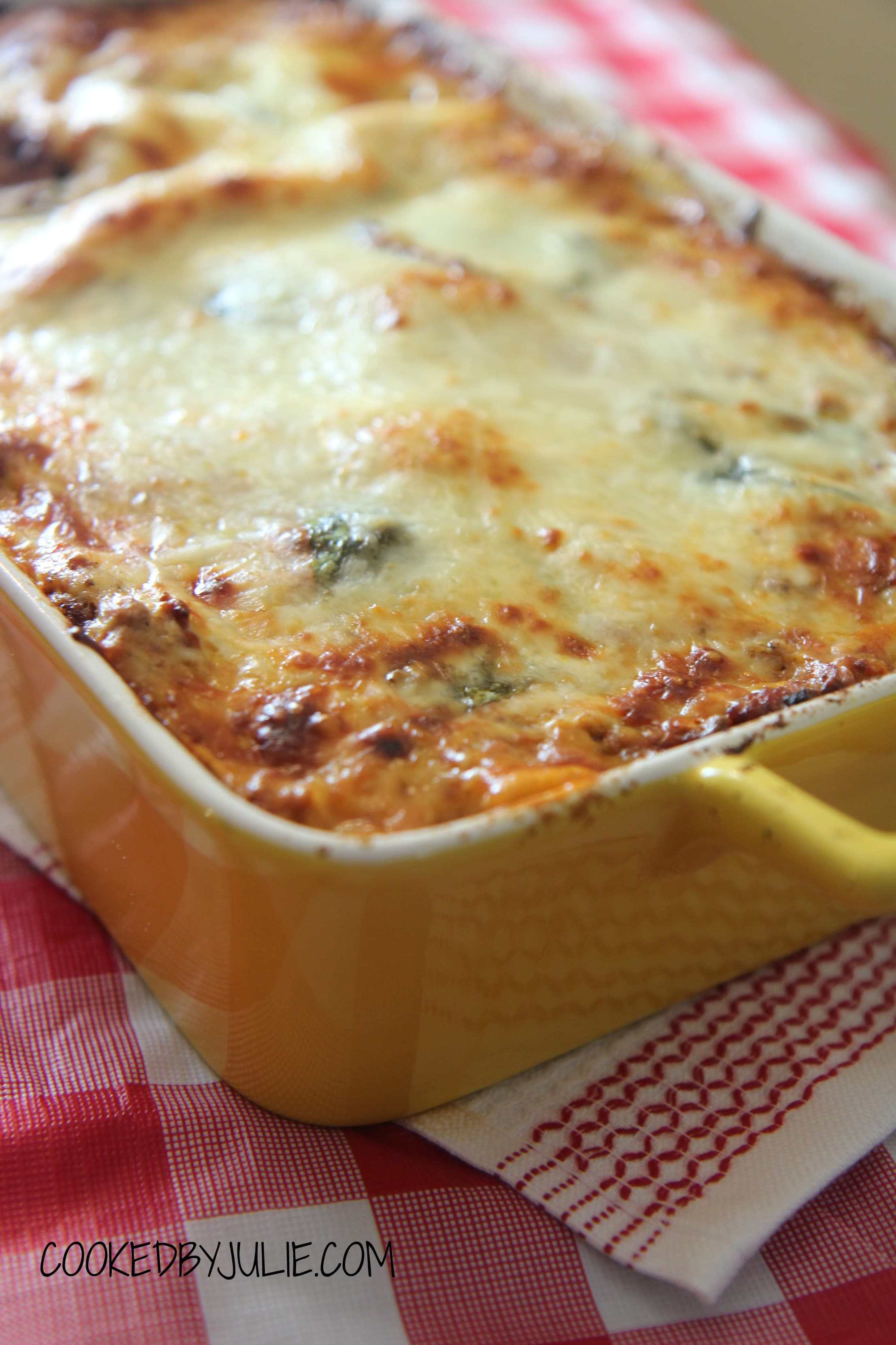 lasagna in a yellow casserole baking dish on top of a white and red towel. 