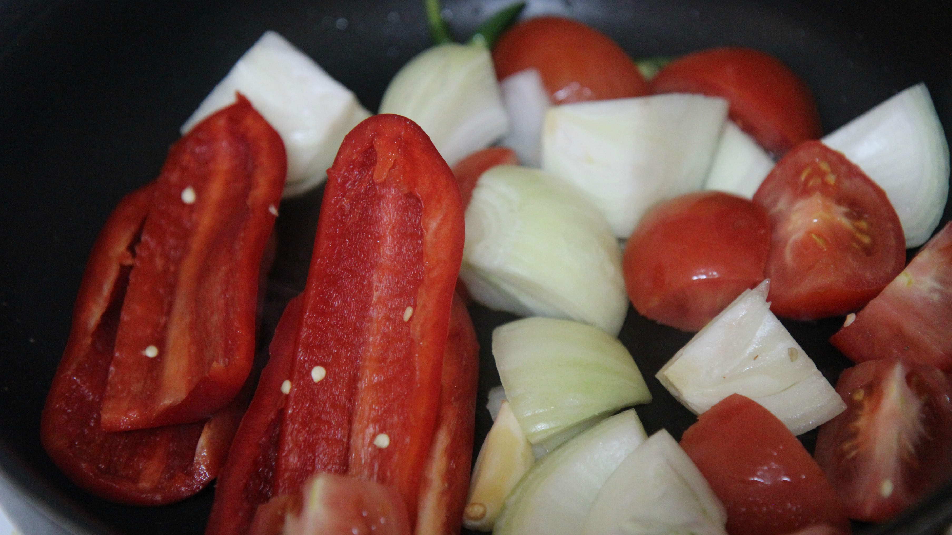 raw peppers, onions, and tomatoes in a black skillet.