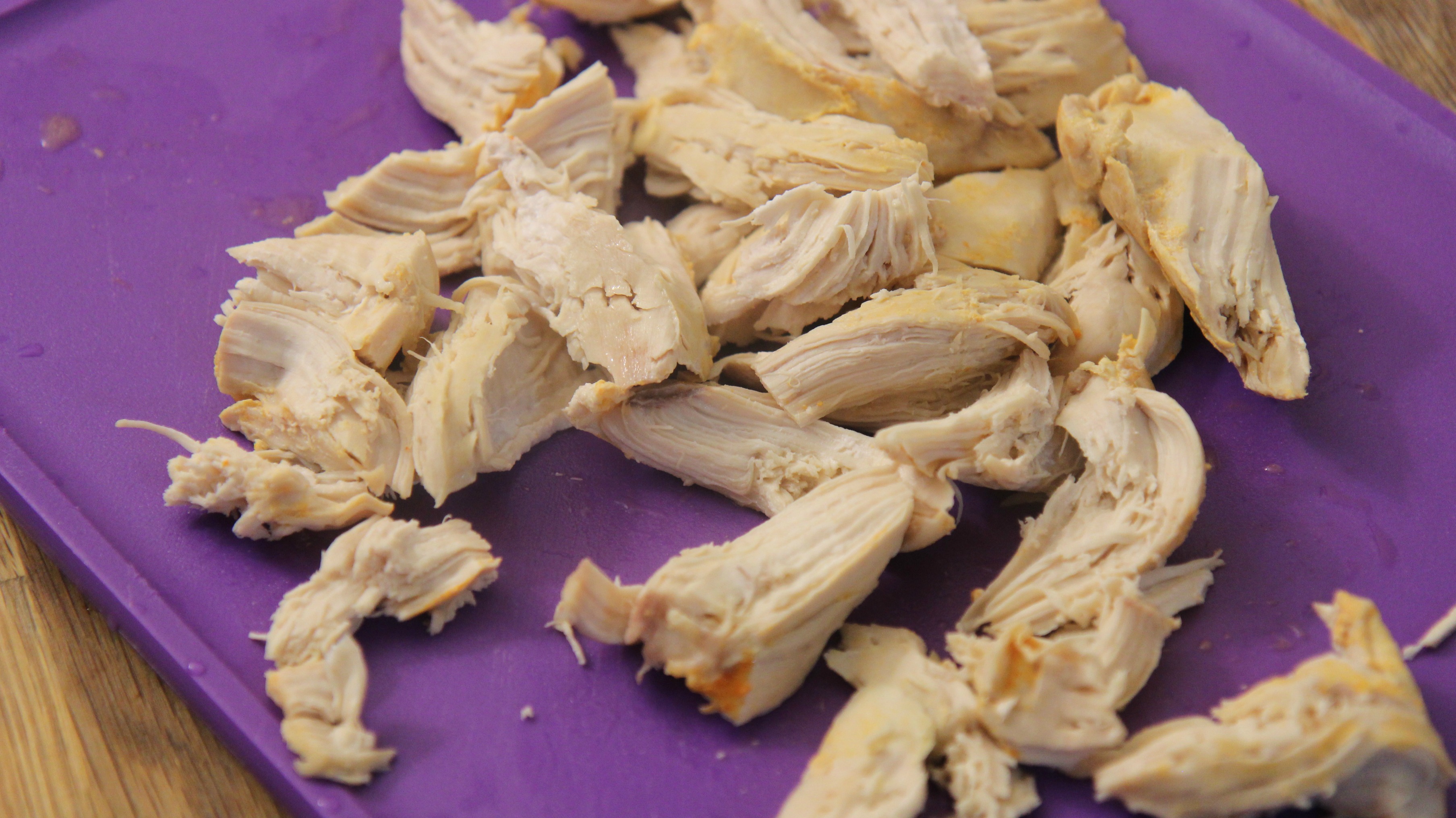 Shredded chicken on a purple cutting board.