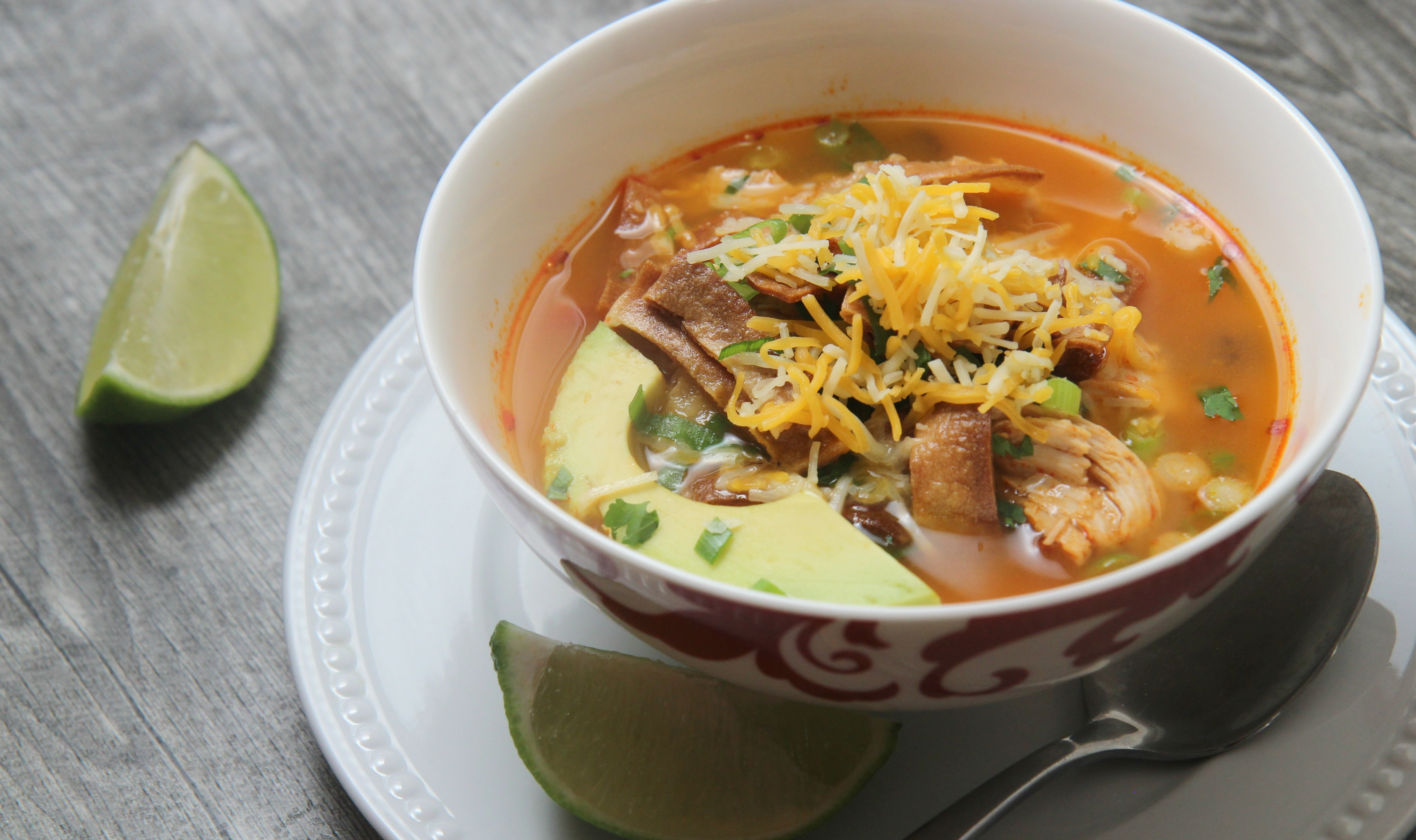 Spicy chicken tortilla soup topped with cheddar cheese and avocado 