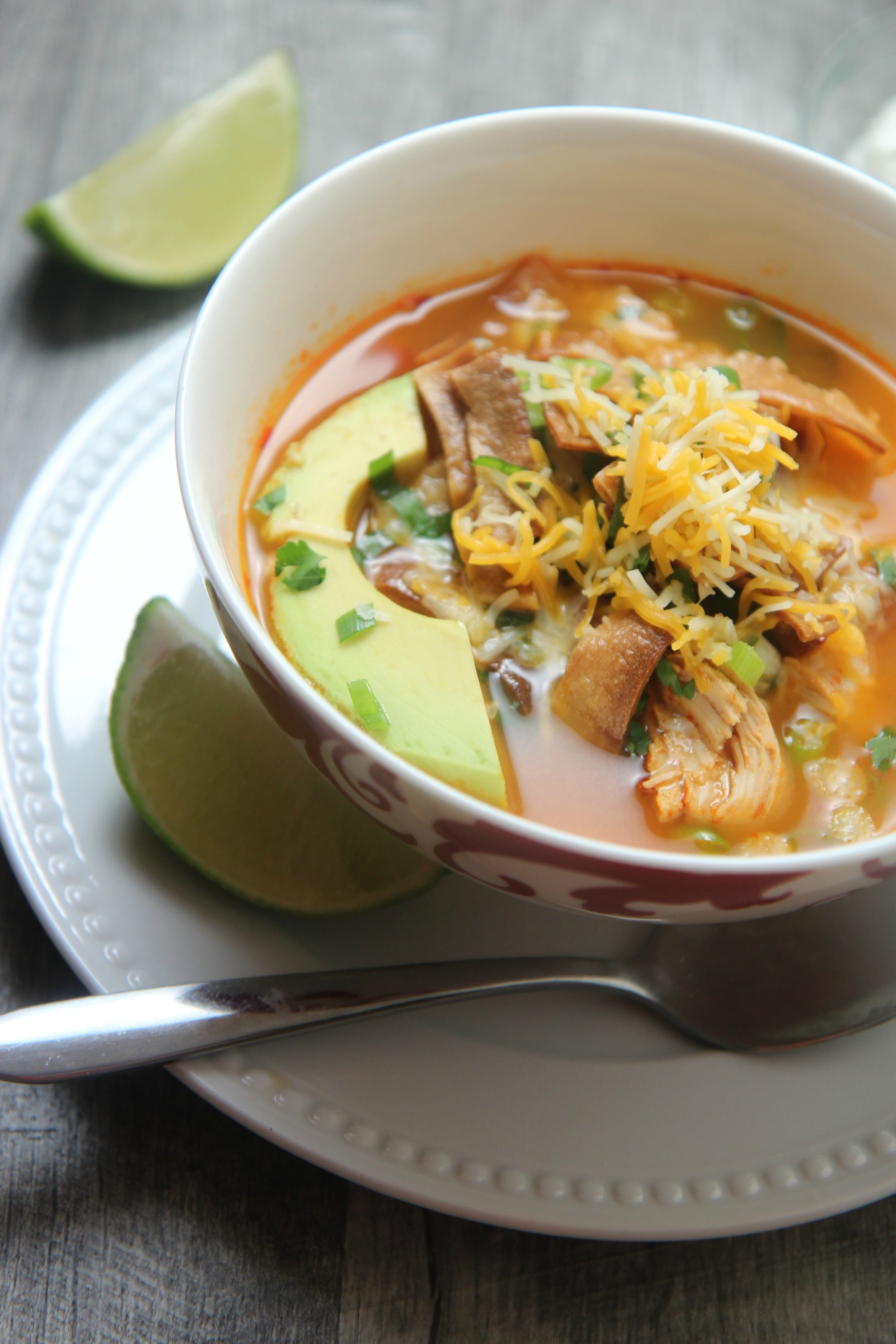 Spicy chicken tortilla soup in a white and red bowl with a spoon
