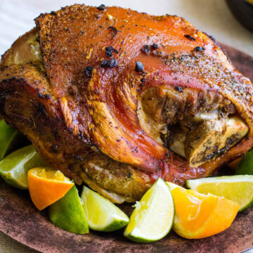 roasted pork on a brown plate with limes and oranges