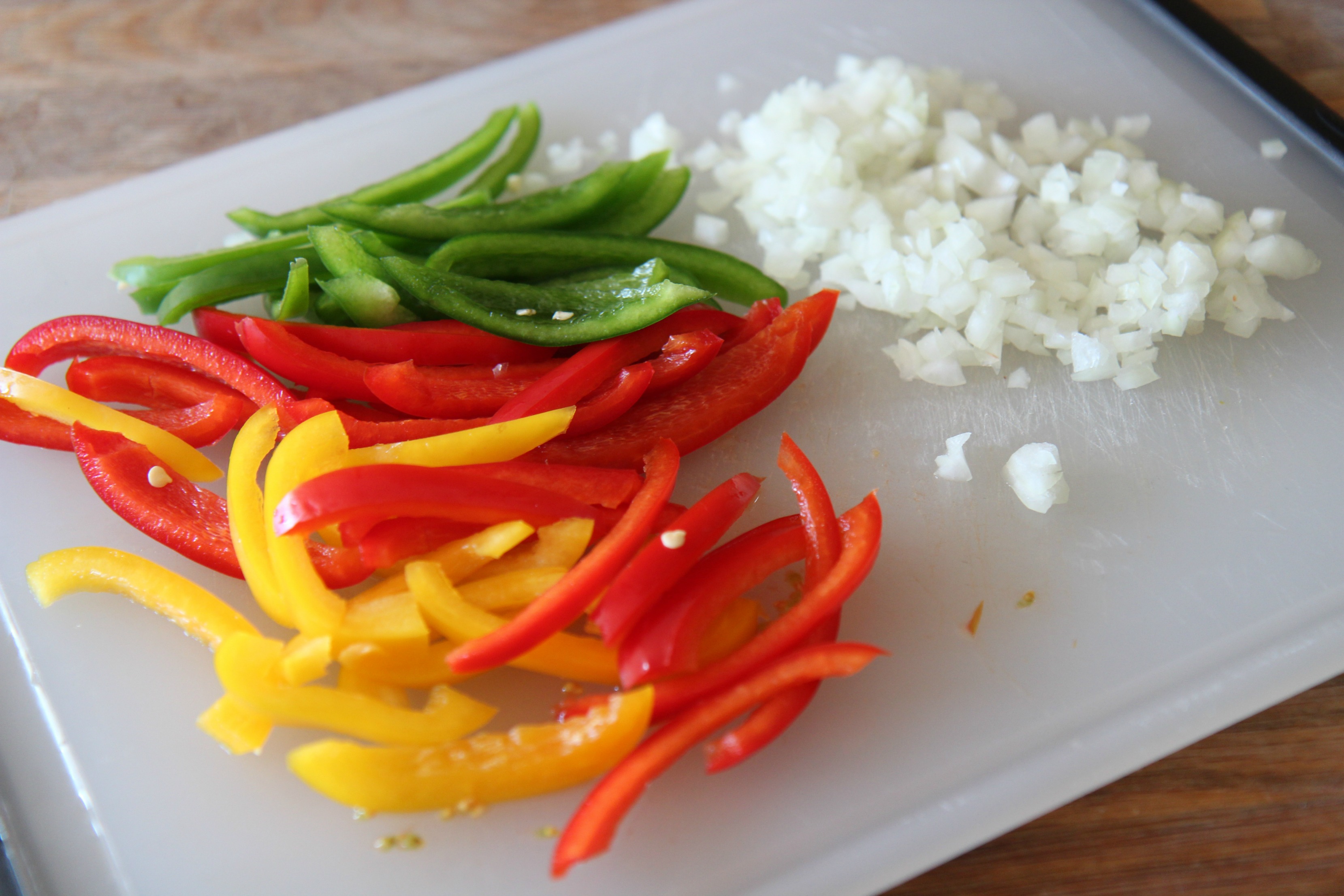 Slice red, yellow, and green bell peppers and dice a small white onion.