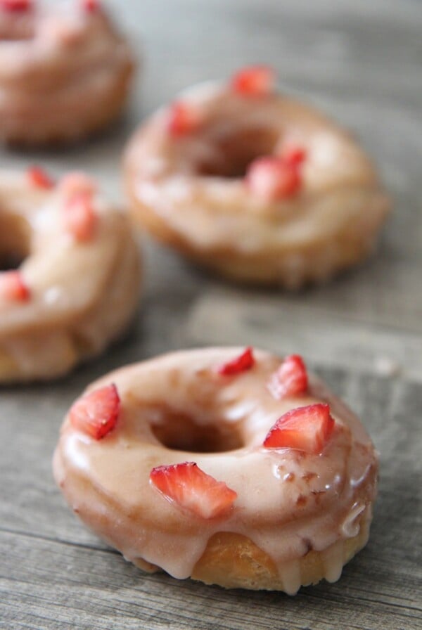 four fresh strawberry donuts on a gray surface.