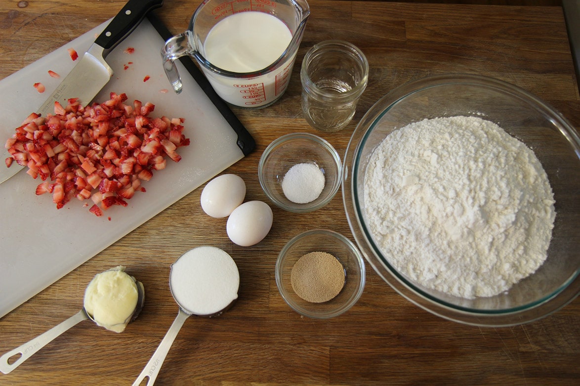 fresh strawberries on a chopping board, milk, eggs, flour, yeast, shortening, and sugar.