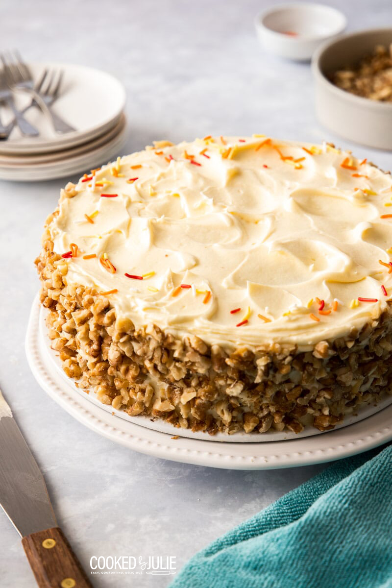 whole carrot cake on a white plate with blue towel on the side 