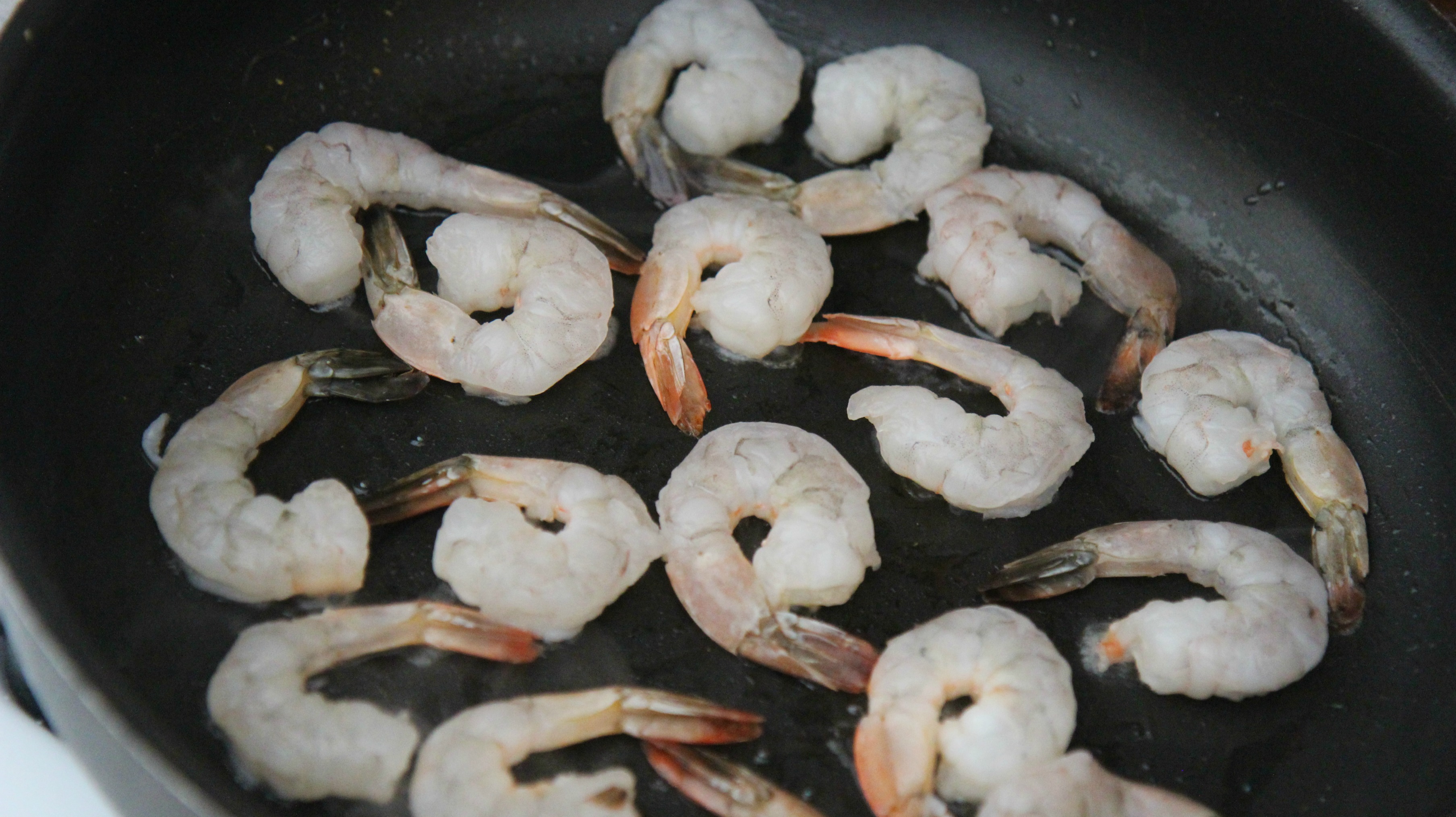 Raw shrimp in a black skillet cooking. 