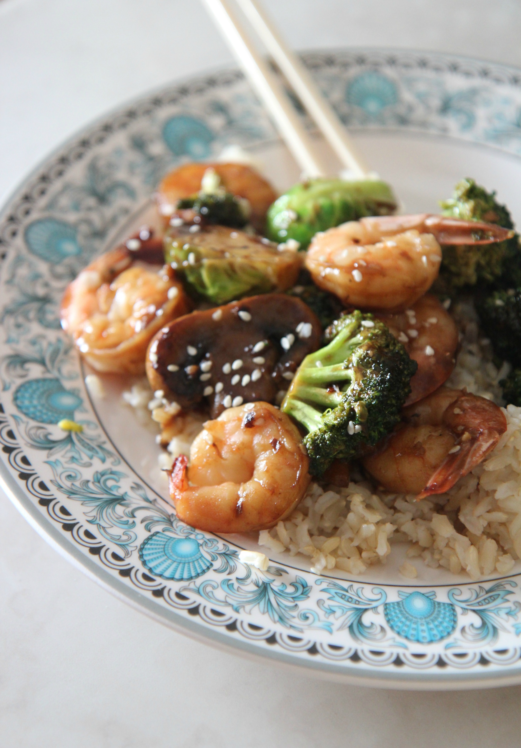 Shrimp, mushrooms, broccoli, and rice on a plate with chop sticks. 