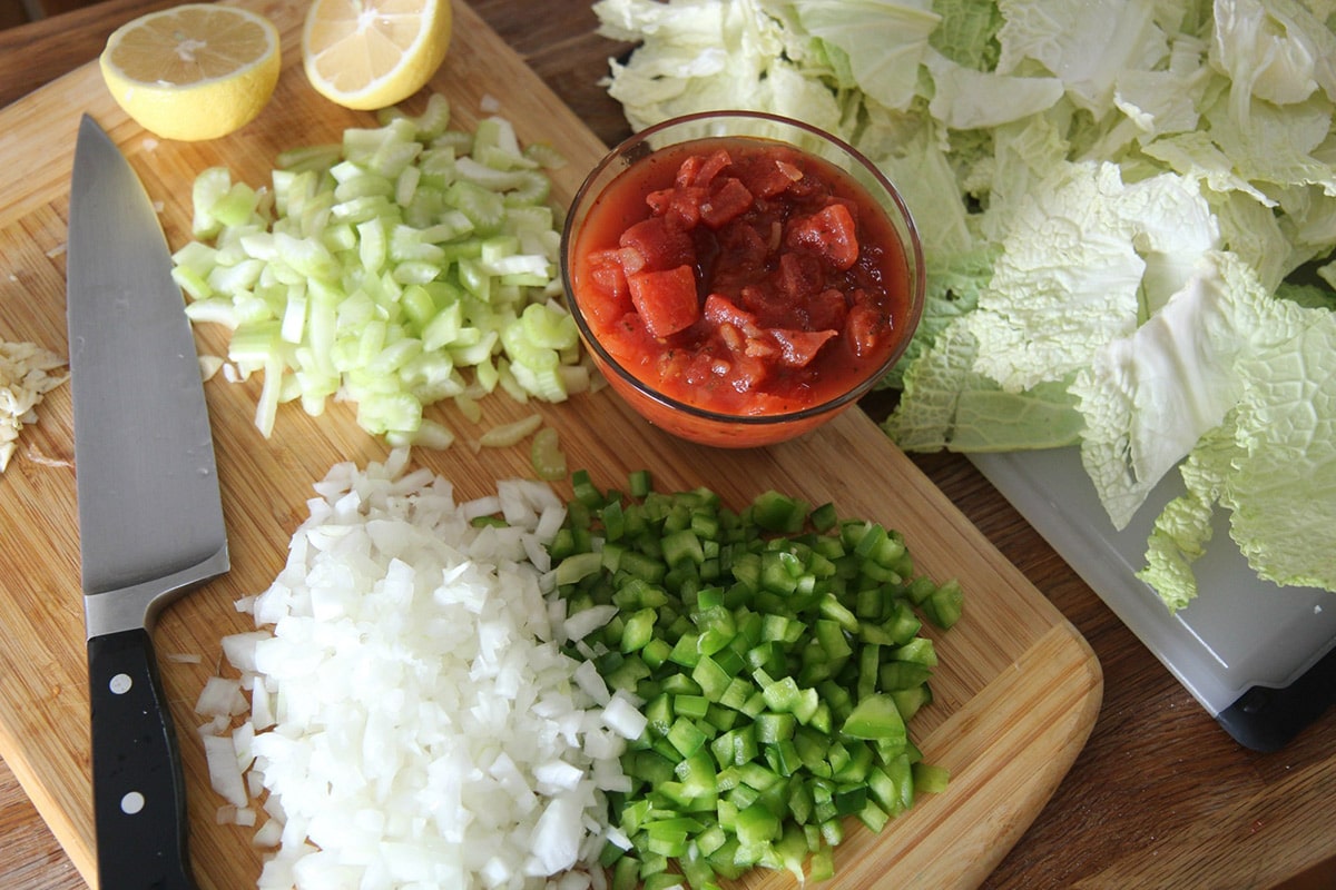 chopped cabbage, onions, tomatoes, lemons, and peppers on a wooden board. 