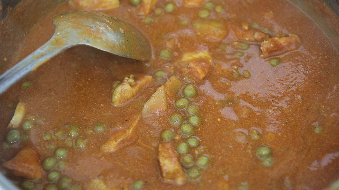curry cooking in a pot with a stainless steel spoon 