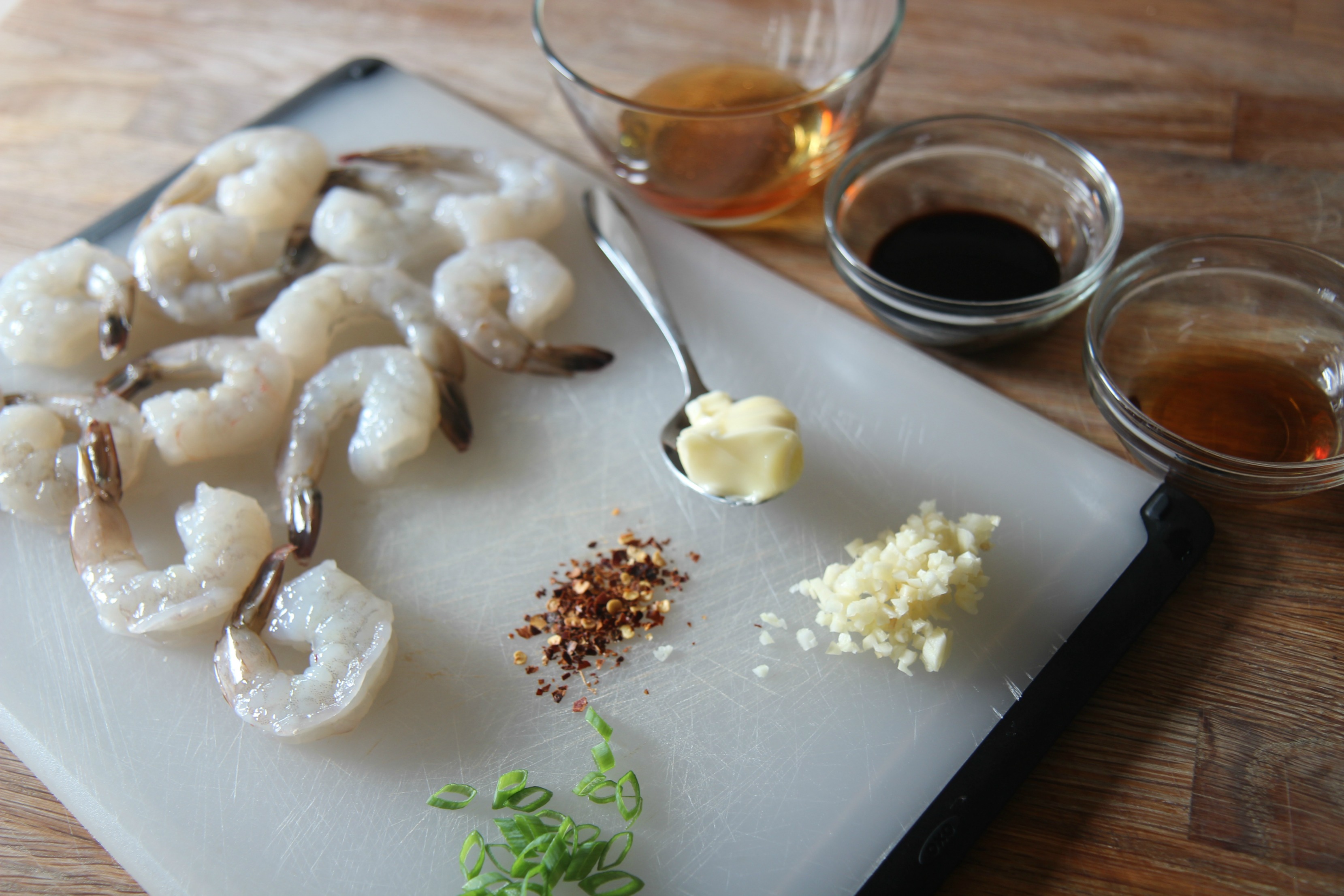 raw shrimp, butter, garlic, sauces, and scallion, on a chopping board. 