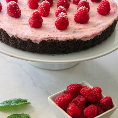 no-bake white chocolate raspberry tart on a white platter with a side of fresh raspberries and mint.