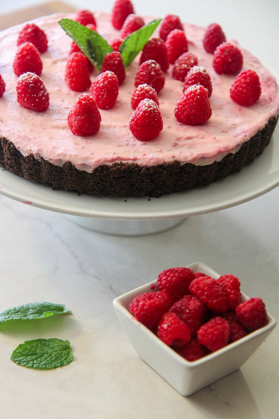 no-bake white chocolate raspberry tart on a white platter with a side of fresh raspberries and mint.