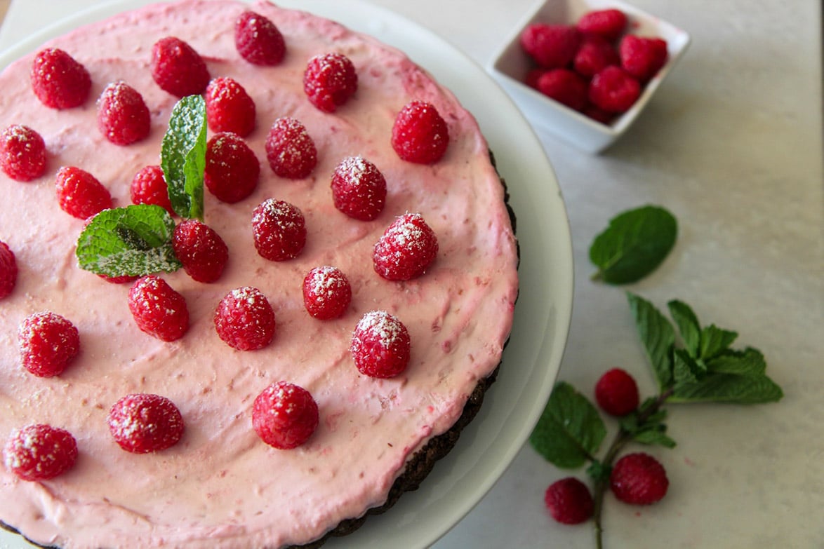 an up close shot of a raspberry tart with mint on the side. 