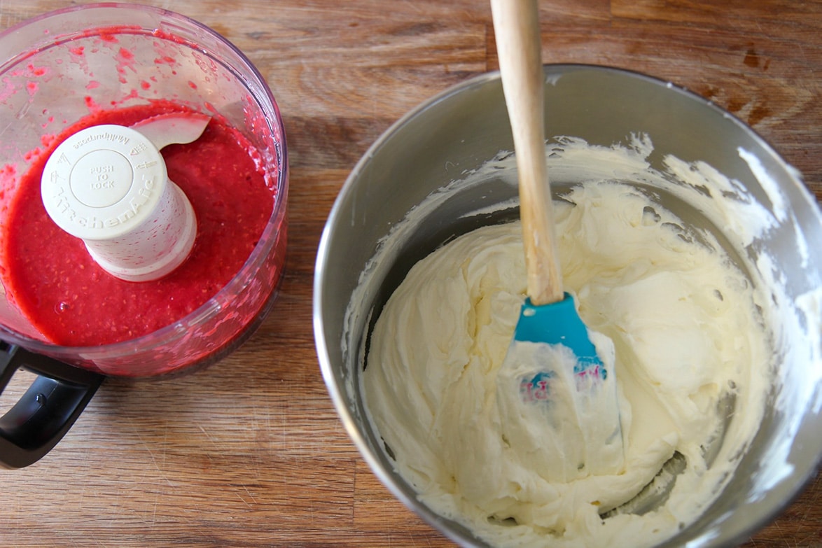 a bowl of whipped cream with a blue spatula and a food processor with raspberry puree.