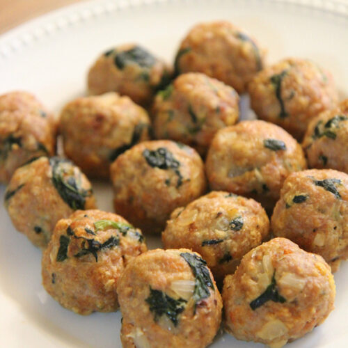 fifteen spinach and turkey meatballs on a white plate.