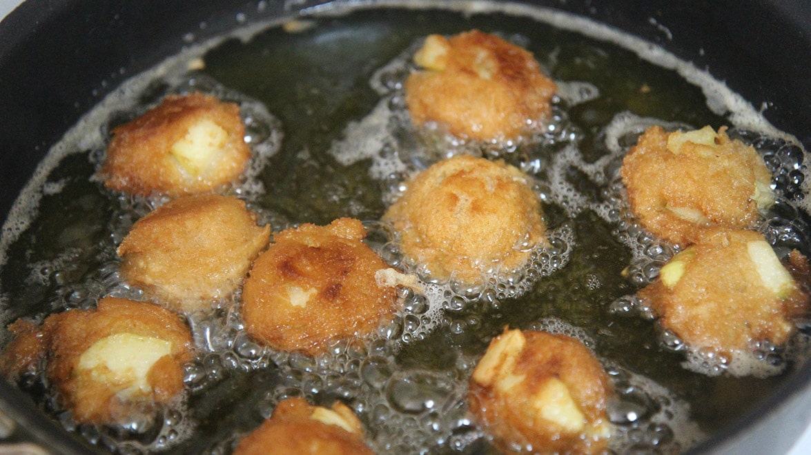 ten apple fritters frying in a skillet with hot oil. 