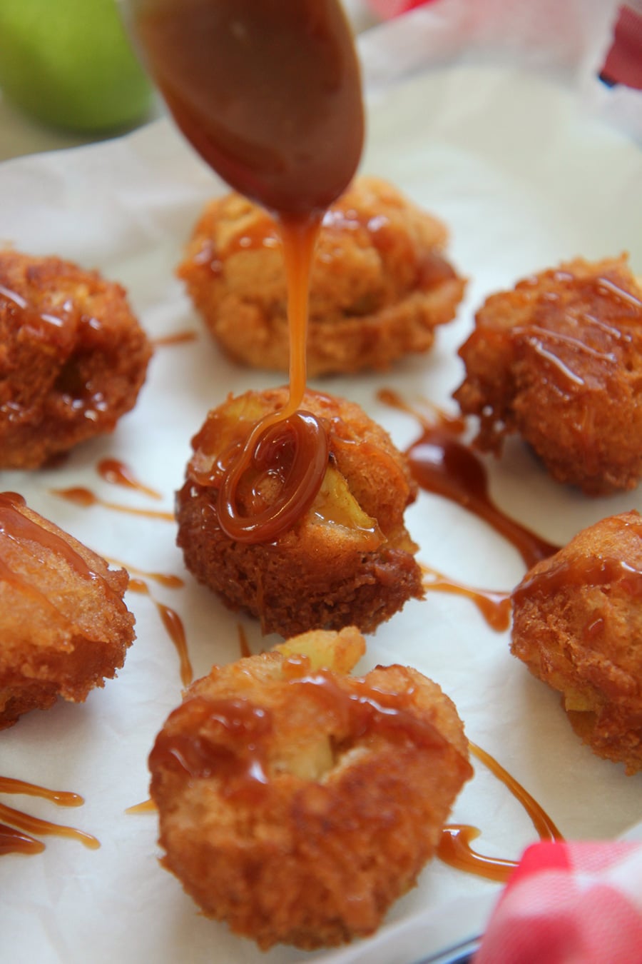 fritters on a white surface with a spoon drizzling caramel sauce on top of one fritter.