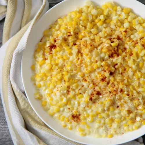 creamed corn in a white plate with a yellow and white kitchen towel on the side.
