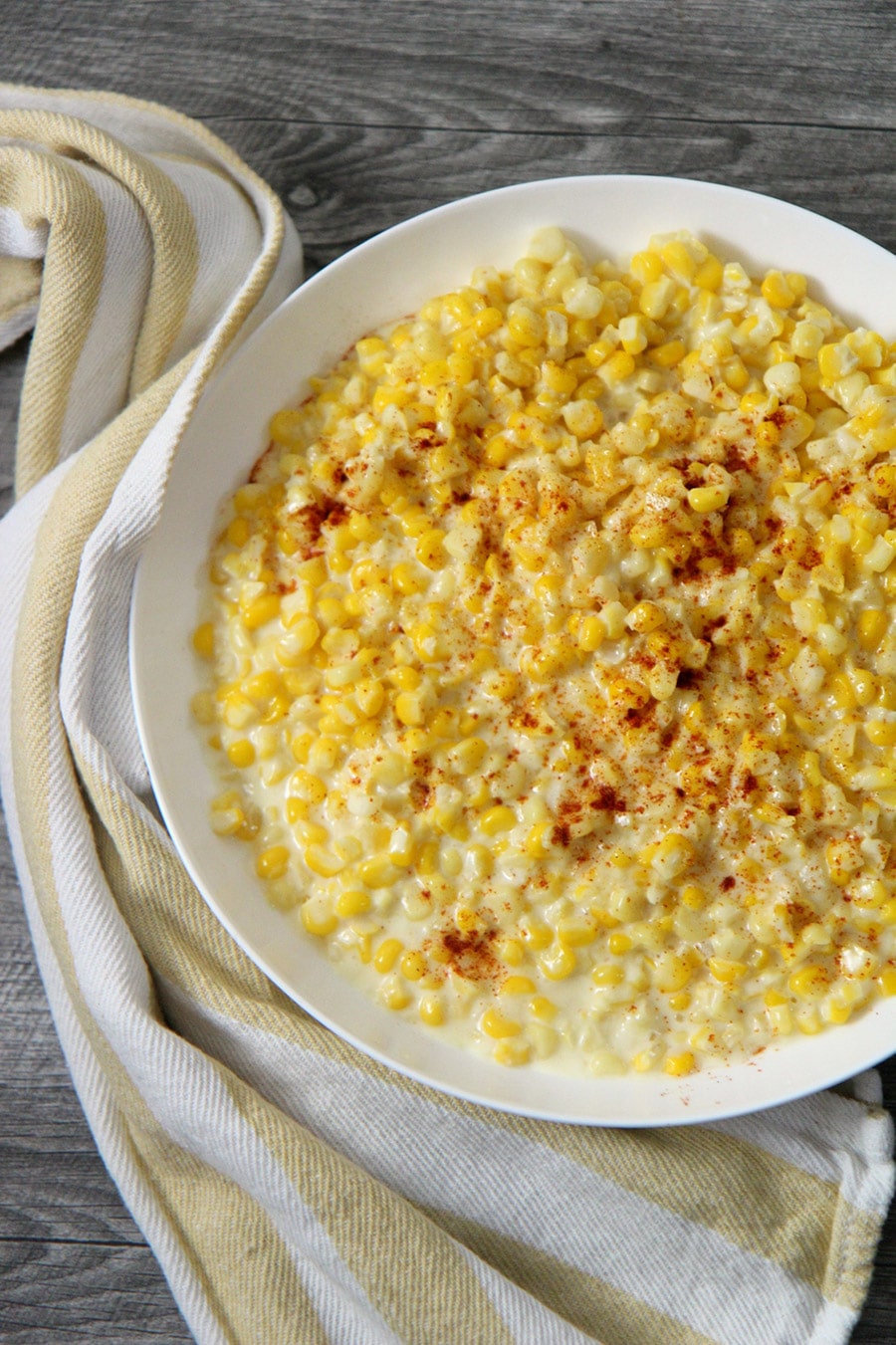 creamed corn in a white plate with a yellow and white kitchen towel on the side.