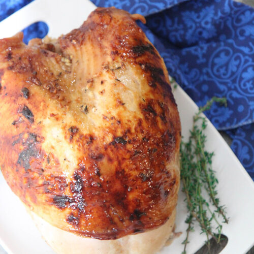 maple glazed turkey breast on a white platter with fresh thyme on the side and a blue towel underneath the platter.