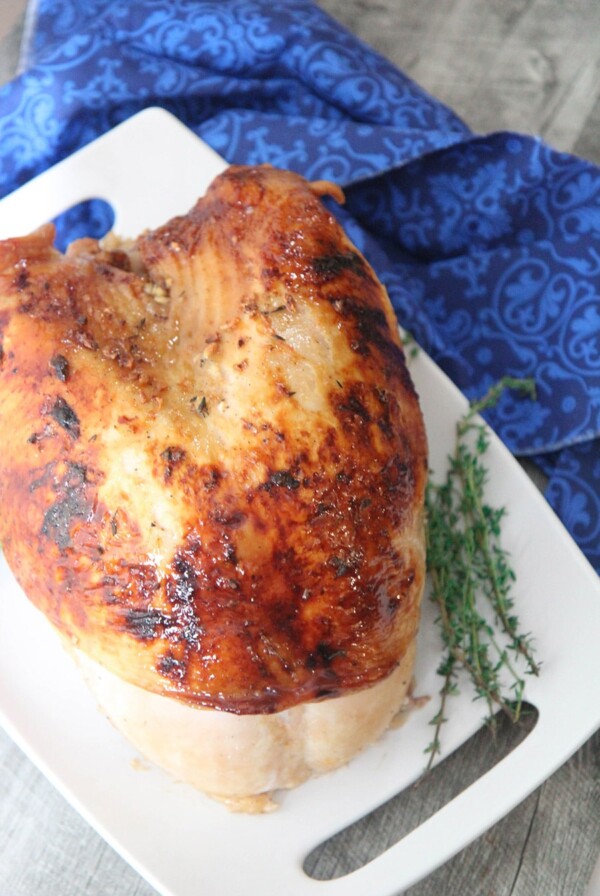 maple glazed turkey breast on a white platter with fresh thyme on the side and a blue towel underneath the platter.