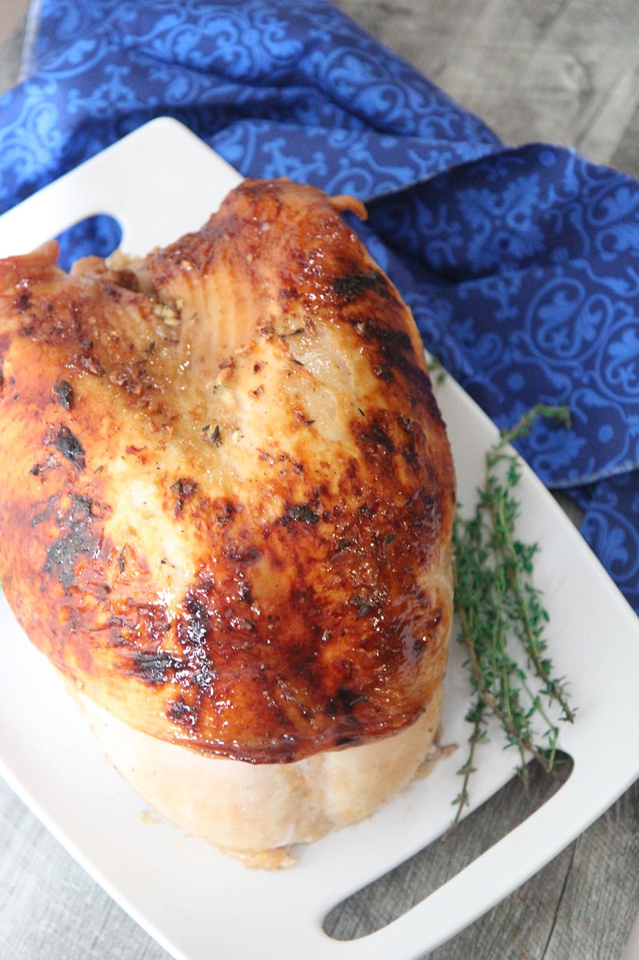 maple glazed turkey breast on a white platter with fresh thyme on the side and a blue towel underneath the platter. 