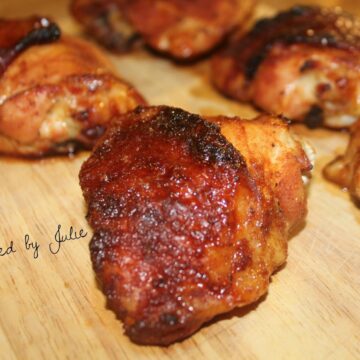 five spicy honey baked chicken thighs on a wooden board. One chicken thigh up close.