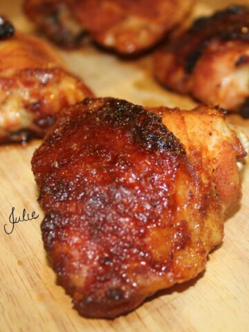 five spicy honey baked chicken thighs on a wooden board. One chicken thigh up close.