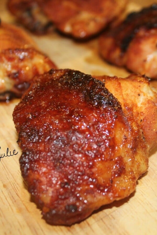 five spicy honey baked chicken thighs on a wooden board. One chicken thigh up close.