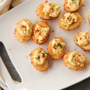nine fried deviled eggs on a white platter with a yellow and white towel on the side.