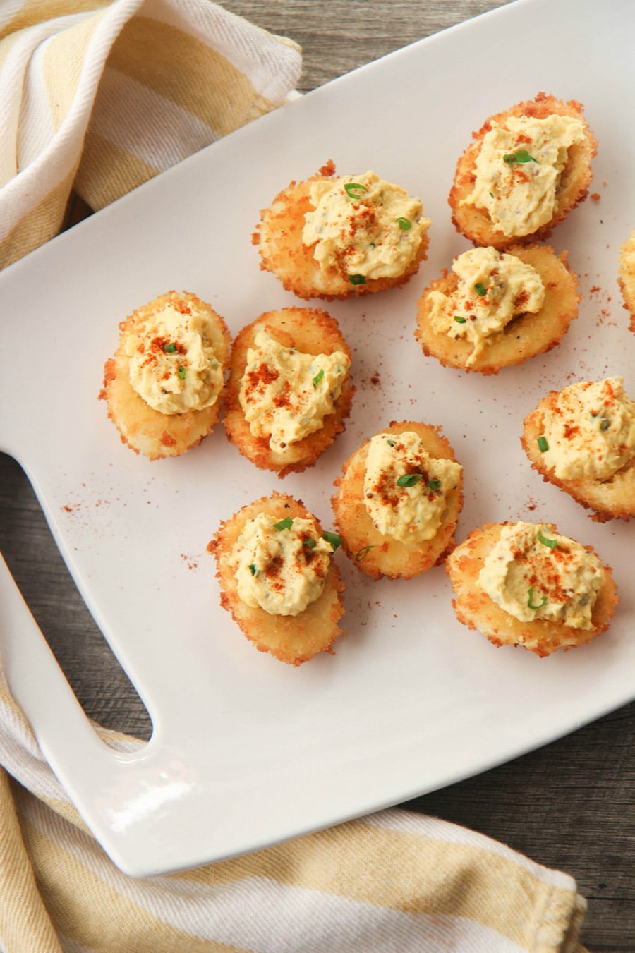 nine fried deviled eggs on a white platter with a yellow and white towel on the side. 