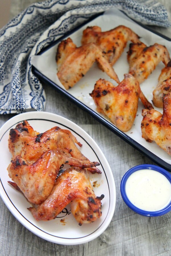 oven roasted chicken wings on a small white plate with a side of blue cheese dip and more chicken wings in the background.