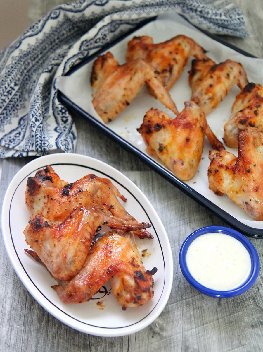 oven roasted chicken wings on a small white plate with a side of blue cheese dip and more chicken wings in the background.