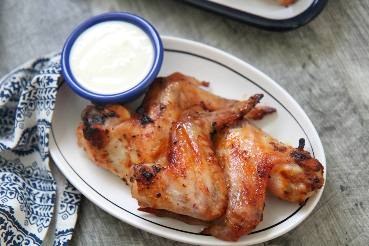 three wings on a white plate with a small side of dipping sauce and a blue and white towel on the side. 