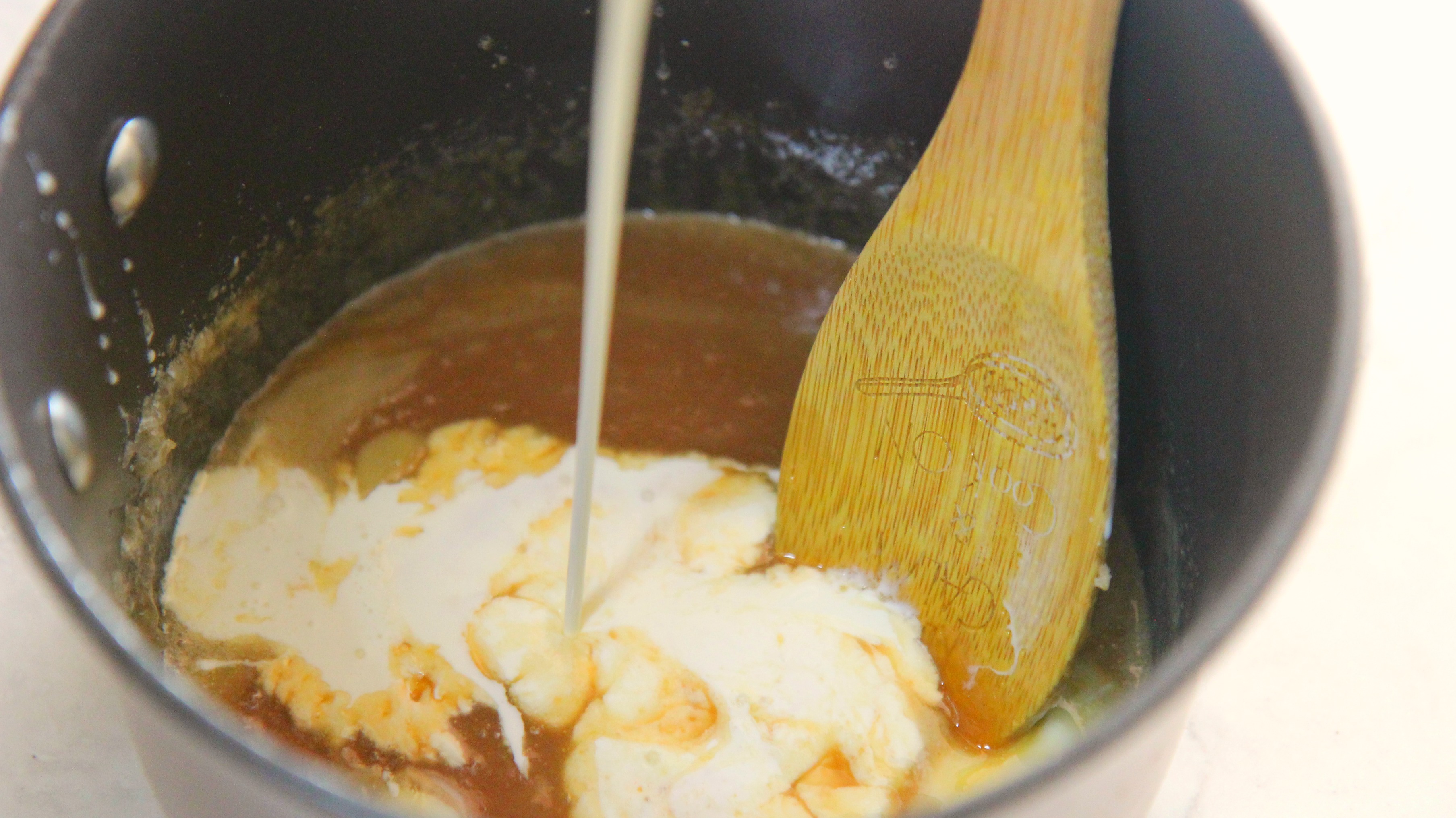 caramel sauce and heavy cream in a sauce pan with a wooden spoon.
