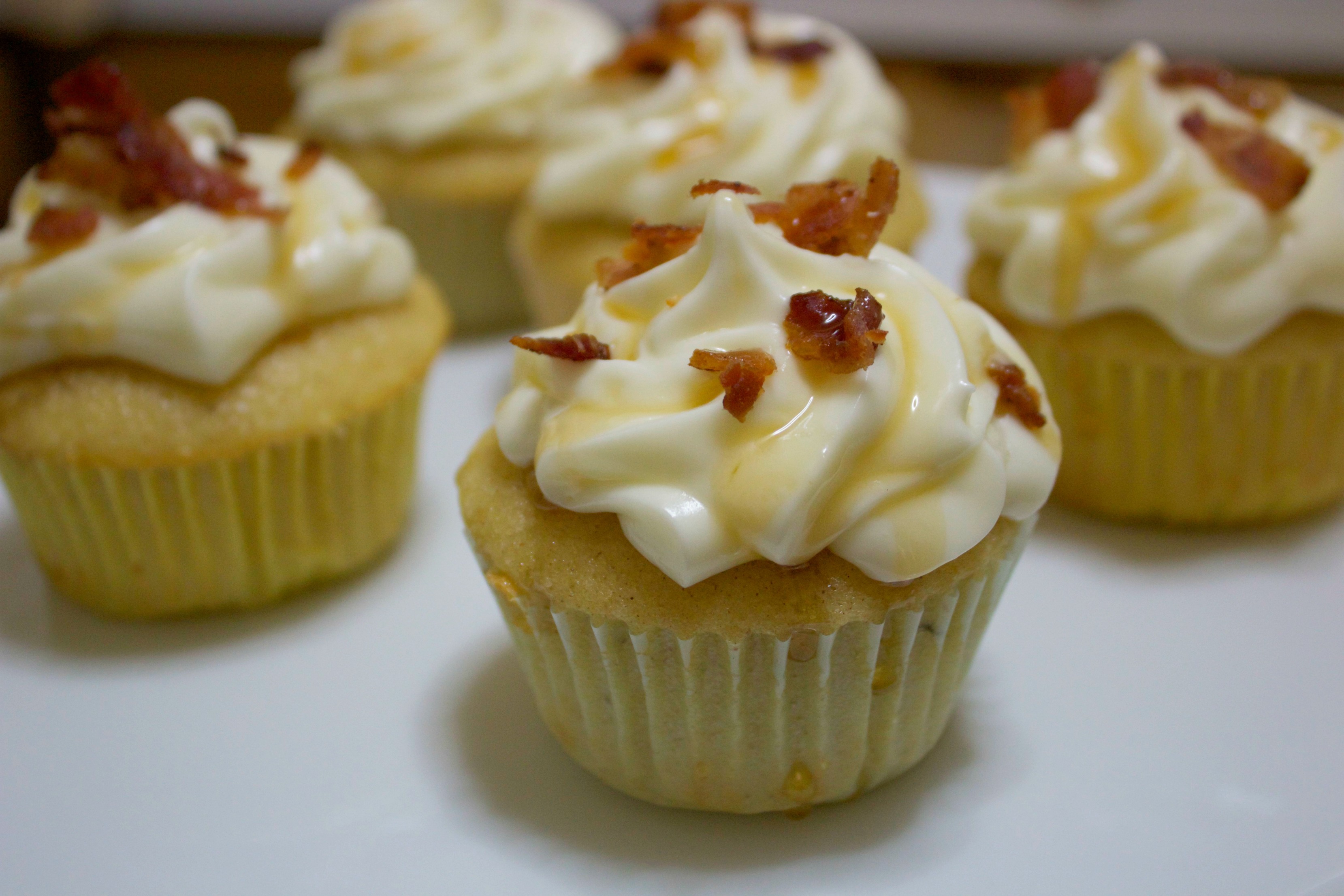 Sweet and savory yellow cupcakes with a cream cheese frosting, syrup drizzle, and bacon bits