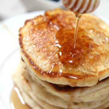 5 stacked pancakes on a plate with a honey comb over it