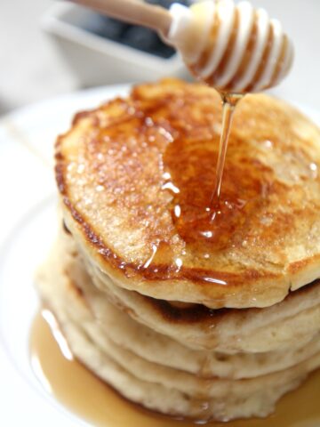 5 stacked pancakes on a plate with a honey comb over it