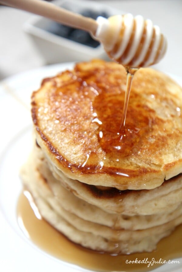 5 stacked pancakes on a plate with a honey comb over it