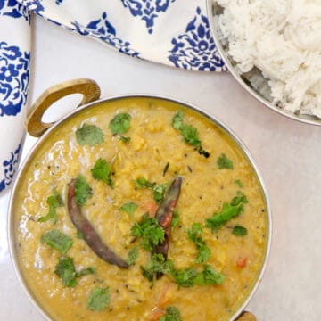 Red Indian style lentils in a small bowl with white rice on the side and a blue and white towel.