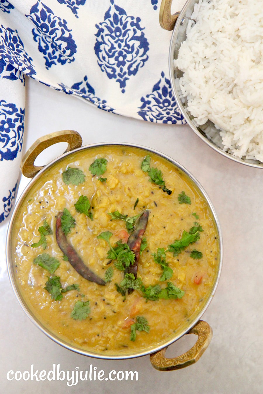 Red Indian style lentils in a small bowl with white rice on the side and a blue and white towel. 