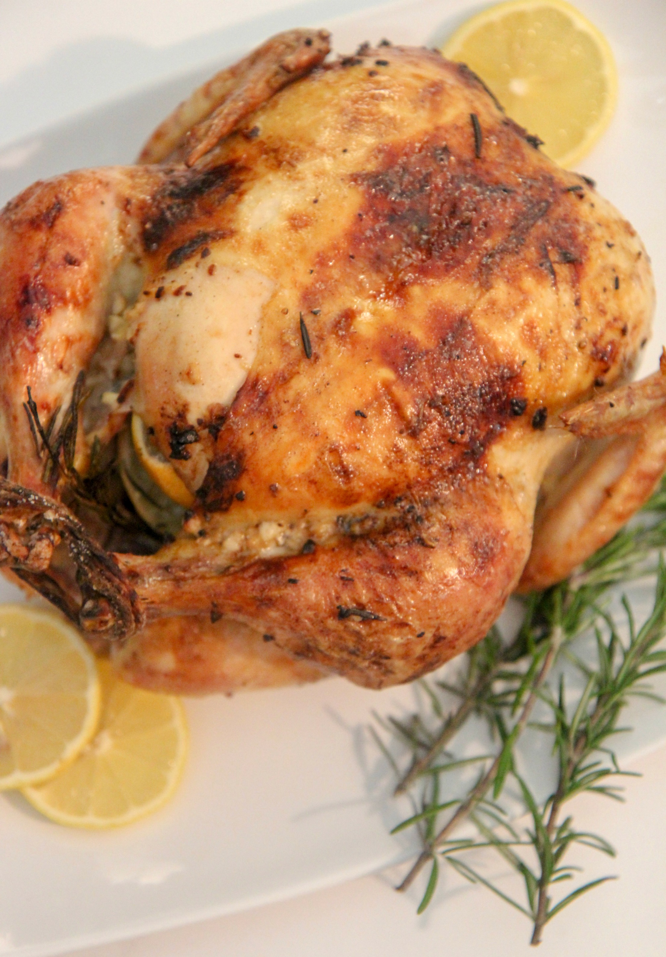 lemon garlic roast chicken on a white platter with rosemary sprigs and lemon slices.