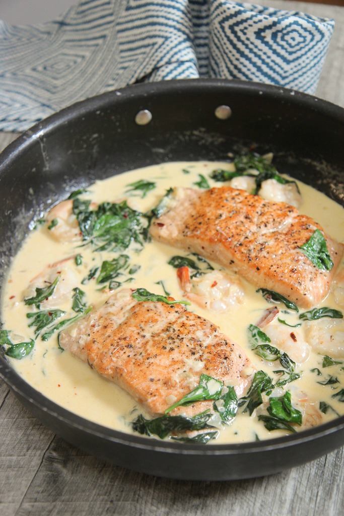 salmon, shrimp, and spinach with a cream sauce in a black skillet. 