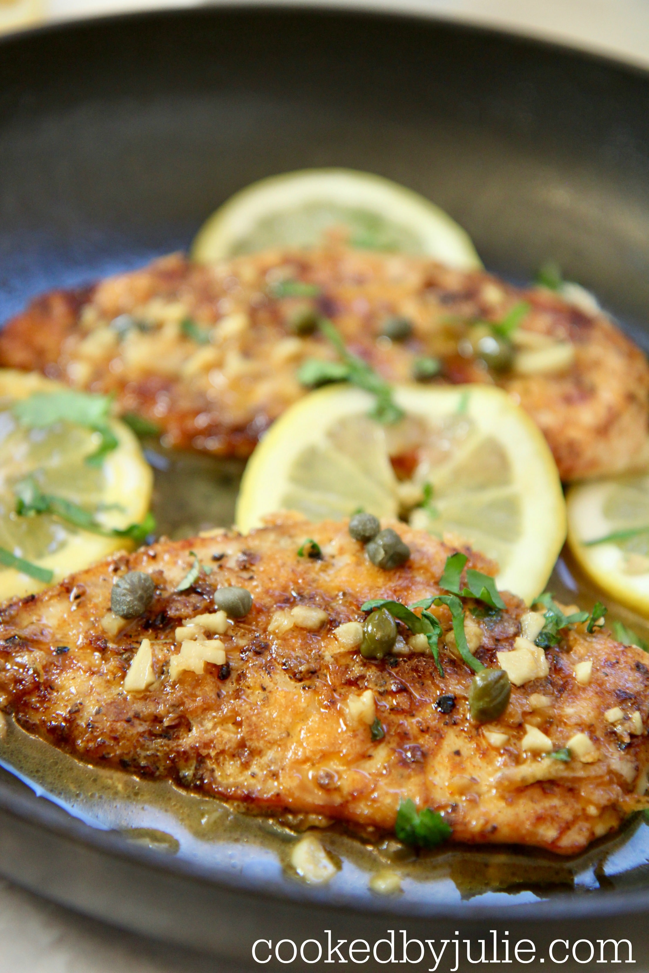 chicken in a skillet with sauce, capers, lemons, and parsley. 